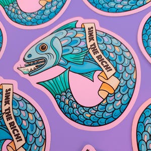 May include: A sticker depicting a blue fish with teal fins and scales, biting a piece of paper. The fish has a banner that reads "SINK THE RICH!" in black text. The sticker is on a pink background with a purple backdrop.