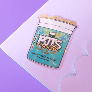 May include: A holographic sticker of a blue and green instant noodle cup with the text "POTS noodle" and "SWEAT & SICK FLAVOUR" with the text "HEART PALPITATIONS IN 4 MINUTES" and "90g".
