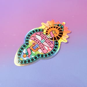 Pu&ograve; includere: Un adesivo olografico con uno schema di colori arcobaleno. L'adesivo presenta una spada con ali e un sole con un alone. Il testo sull'adesivo recita "Migraine Warrior".