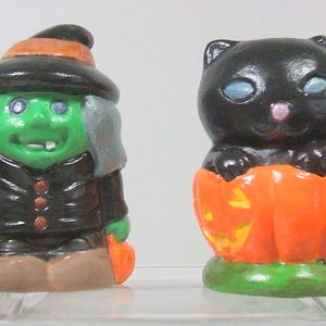 May include: Two Halloween themed figurines. A green witch with a black hat and broom, and a black cat sitting in a jack-o-lantern.