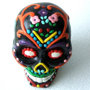 May include: A black sugar skull with colorful floral and geometric designs painted on it. The skull has red, orange, yellow, green, blue, purple, and white paint.