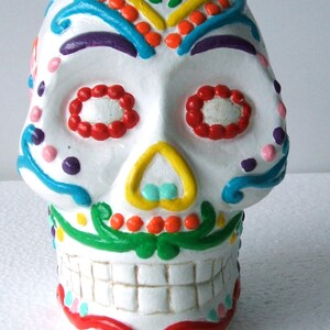 May include: A white ceramic skull with colorful painted details, including flowers, swirls, and dots. The skull has a painted smile and teeth.
