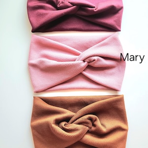 May include: Three fabric headbands in different colors: burgundy, pink, and brown. The headbands are twisted and have a waffle texture.