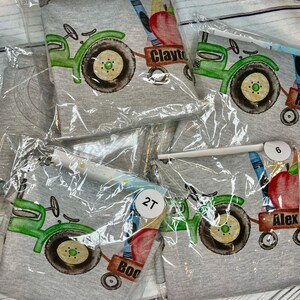 May include: Four gray t-shirts with a green tractor design, a red apple, and school supplies. The shirts have the names Clayton, Alex, Boo, and 2T printed on them.