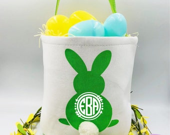May include: Green Easter bunny-shaped canvas tote bag with a white monogram "EBA" in a circle. The bag is filled with colorful plastic Easter eggs and has a green handle.