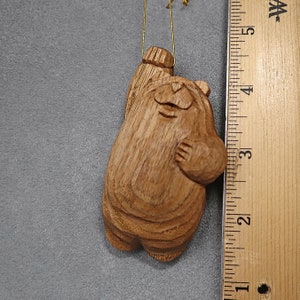 May include: A wooden carved bear ornament with a gold string for hanging. The bear is standing on its hind legs with its arms raised. The bear is painted in a natural wood color.
