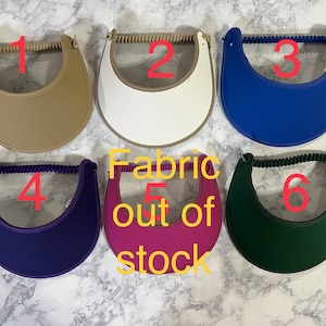 May include: Six different colors of sun visors with a fabric strap. The visors are numbered 1 through 6. Fabric 5 is out of stock.
