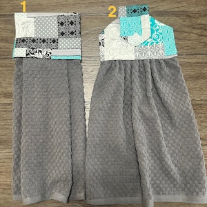 May include: Two gray kitchen hand towels with decorative patchwork tops. One towel features a patchwork design with black, white, and gray patterns, while the other has a turquoise, white, and gray patchwork design.