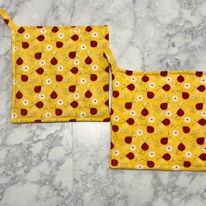 May include: Two yellow pot holders with a pattern of red ladybugs and white flowers.