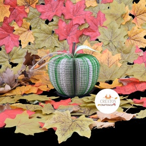 May include: A green book-shaped apple made from pages of a book, surrounded by fall leaves. The apple is a handmade craft and has a green ribbon tied around it. The image also includes a white circle with the text "Creaton Crafts & Gifts".