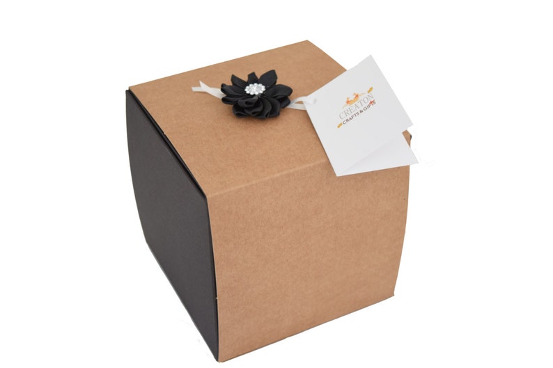 May include: A brown cardboard gift box with a black ribbon and a black flower with a rhinestone center. The box has a white tag attached with the text "Creations Crafts & Gifts".