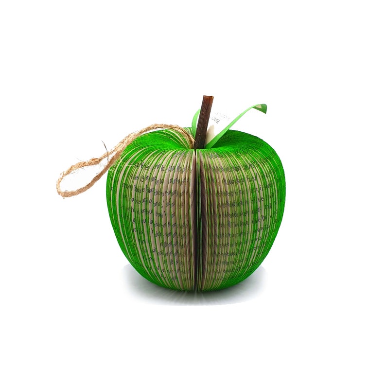 May include: A green apple made from folded pages of a book. The apple has a brown twig stem and a green leaf.