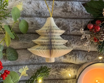 May include: A white paper Christmas tree ornament with a gold string for hanging. The tree is made from folded pages of a book.