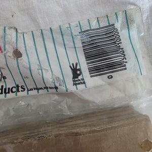 May include: A partially visible package with a barcode and the text "Made in America". The packaging has a white background with teal vertical stripes. The bottom portion of the package contains a stack of brown paper.