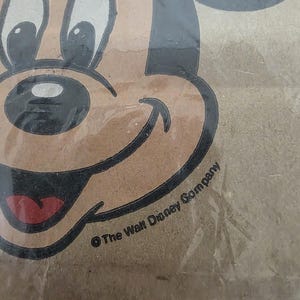 May include: Close-up of a vintage Mickey Mouse image. The image features Mickey's face with black outlines, a brown face, white eyes, and a red tongue. The text "&copy; The Walt Disney Company" is visible.