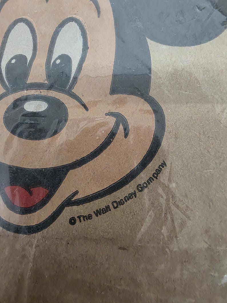 May include: Close-up of a vintage Mickey Mouse image. The image features Mickey's face with black outlines, a brown face, white eyes, and a red tongue. The text "&copy; The Walt Disney Company" is visible.