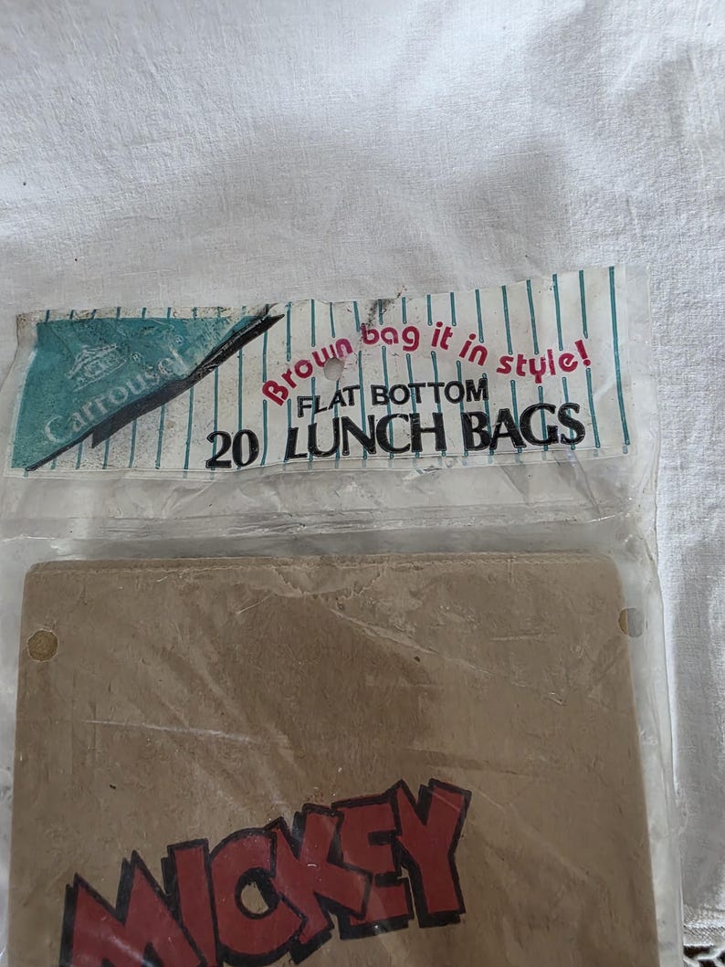 May include: A package of 20 flat-bottom lunch bags. The packaging includes the text "Brown bag it in style!" and "Carousel". The bags are brown with the word "Mickey" in red.