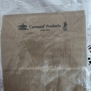 May include: A brown paper bag with the text "Carousel Products" and a carousel logo. The bag is sealed in a clear plastic bag. The text "Made in America" is also visible.