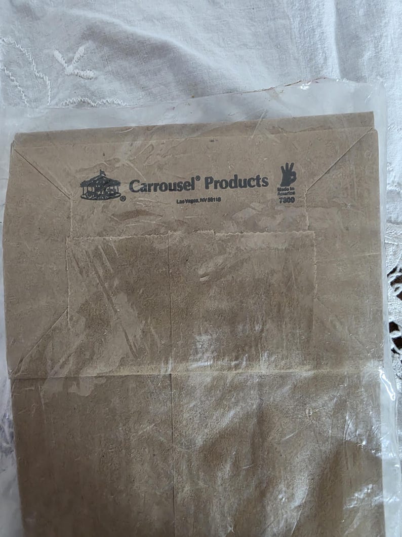May include: A brown paper bag with the text "Carousel Products" and a carousel logo. The bag is sealed in a clear plastic bag. The text "Made in America" is also visible.