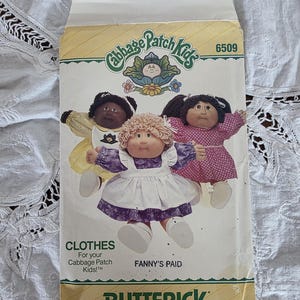 May include: A vintage Butterick sewing pattern envelope for Cabbage Patch Kids clothes. The envelope features illustrations of three Cabbage Patch Kids dolls in various outfits. The text includes "CLOTHES" and "FANNY'S PAID".