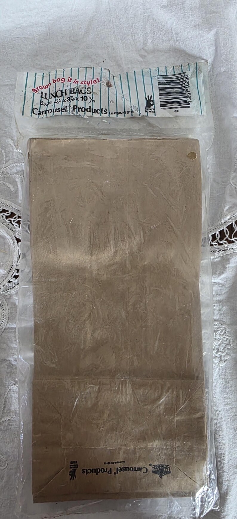 May include: A package of brown paper lunch bags, 5 5/8 x 3 x 10 inches, sealed in clear plastic. The packaging includes text that reads "Brown bag it in style!" and "Carrousel Products."