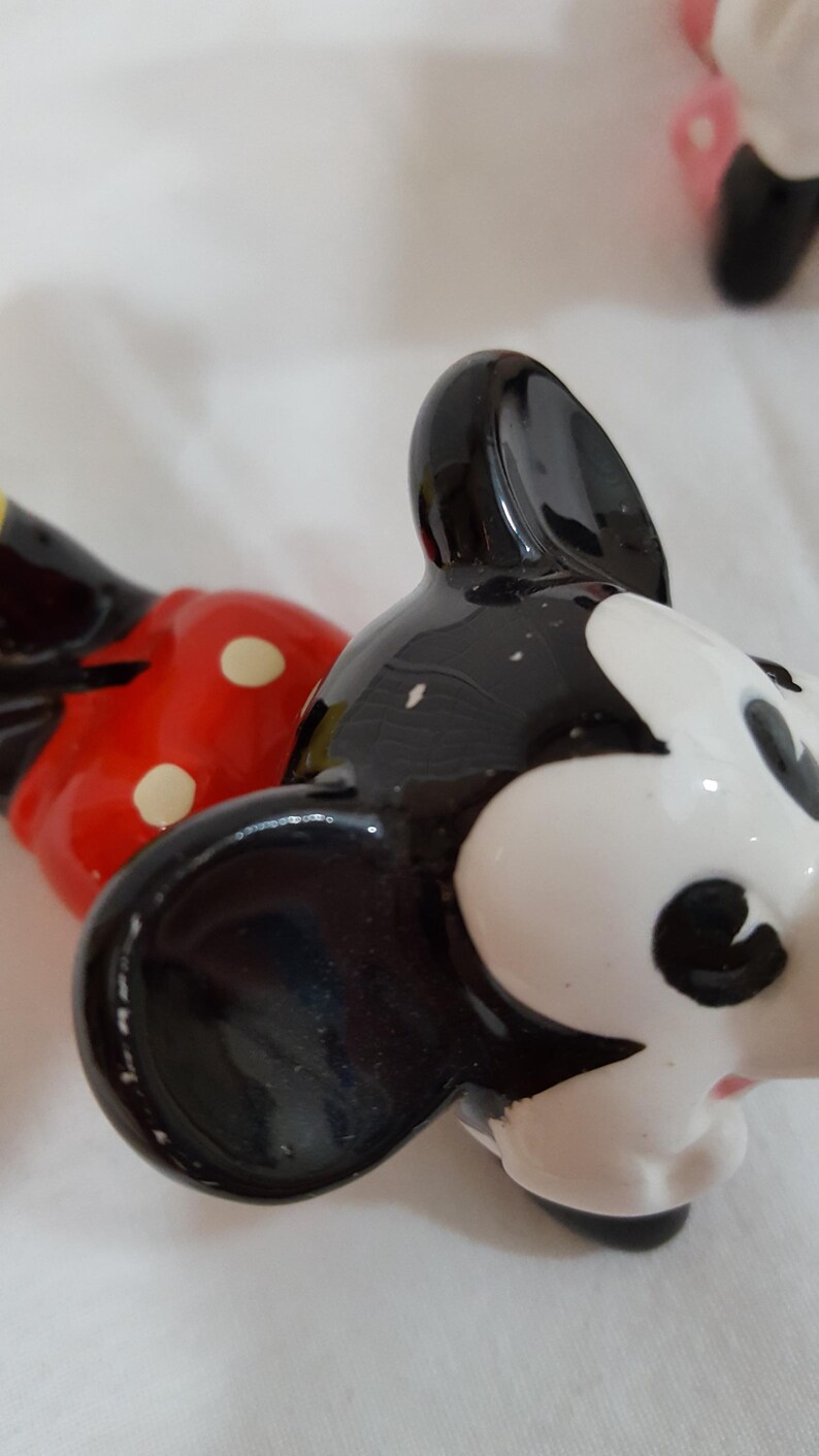 Może przedstawiać: Zbliżenie ceramicznej figurki Myszki Miki. Figurka ma czarną głowę z białymi rysami twarzy i dużymi czarnymi uszami. Czerwony element w białe grochy jest widoczny w tle.