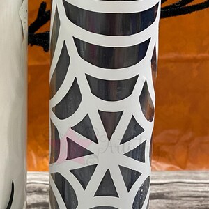 May include: A black glass candle with a white spiderweb design. The candle is in a clear glass jar.