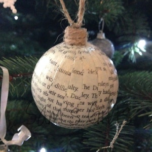 Könnte beinhalten: Ein weißer Weihnachtsbaumschmuck, der mit gedrucktem Text aus einem Buch bedeckt ist. Der Schmuck hängt an einem grünen Weihnachtsbaum.