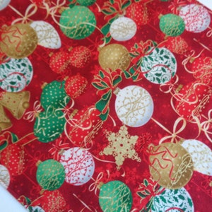 Könnte beinhalten: Ein roter Stoff mit einem sich wiederholenden Muster aus Weihnachtsornamenten in Gold, Grün und Weiß. Das Design umfasst kugelförmige Anhänger mit Punkten, Schnörkeln und floralen Motiven, durchsetzt mit goldenen Schneeflocken und Glocken.