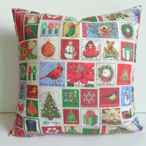 May include: Square Christmas-themed pillow with a patchwork design. The pillow features a collage of festive images, including ornaments, a snowman, a Christmas tree, and state names. The color scheme includes red, green, and white.