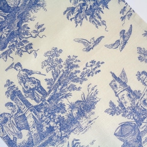Puede incluir: Una tela con un estampado toile de Jouy azul y blanco. El diseño representa figuras, árboles y edificios en una escena pastoral. Dos pájaros vuelan en el cielo. La tela tiene un fondo crema claro.