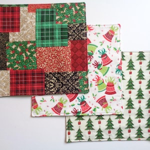 Puede incluir: Un conjunto de cuadrados de tela con temática navideña. Uno presenta un diseño de patchwork con patrones rojos, verdes y beige. Los otros dos cuadrados tienen estampados festivos de campanas y árboles de Navidad, ideales para la decoración.