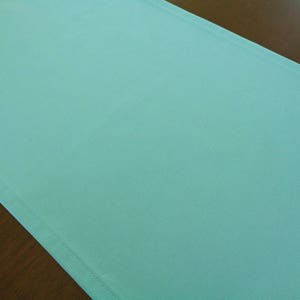 May include: A solid turquoise table runner. The runner is made of a smooth, soft fabric.