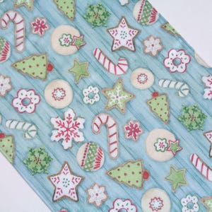 May include: A light blue fabric featuring a repeating pattern of Christmas-themed cookies, including red and white candy canes, green and white Christmas trees, red and white snowflakes, and round cookies with red and green decorative icing.