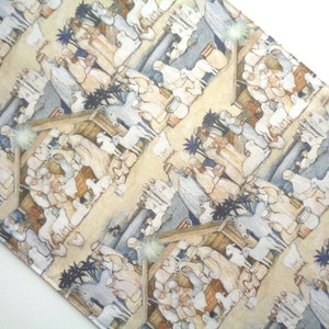 May include: A beige fabric with a repeating pattern depicting a Nativity scene. The illustration features figures, animals, and structures in muted tones, with a starburst element. The overall theme is religious and festive.