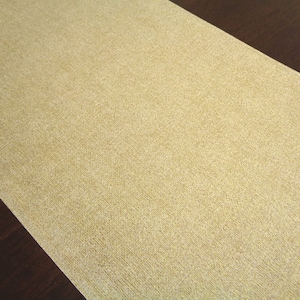 May include: A close-up of a gold glitter table runner. The runner has a subtle shimmer and a textured surface.
