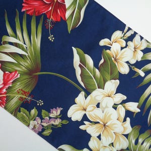 May include: A navy blue fabric with a tropical floral pattern. The design features large red hibiscus flowers, white plumeria, and green palm leaves. The fabric is suitable for various craft projects.