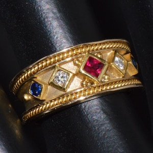 May include: A gold band ring with a braided design and five square-shaped gemstones. The gemstones are red, blue, and white.