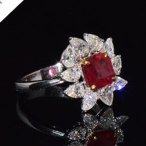 Peut inclure: Une bague en argent ornée d'un grand rubis central carré, entouré d'un halo de diamants en forme de poire et ronds. La bague est présentée sur un fond noir, avec le logo GIA en haut à gauche.