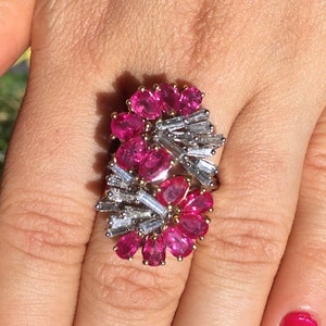 May include: A ring featuring a cluster of pink gemstones and baguette-cut diamonds set in a gold band.