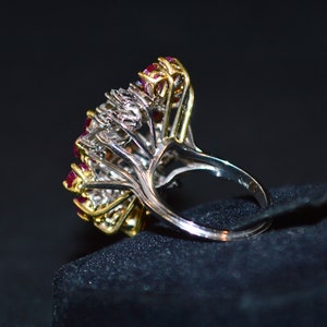 May include: A silver and gold ring featuring a cluster of red rubies and white diamonds. The ring is displayed on a black velvet background.