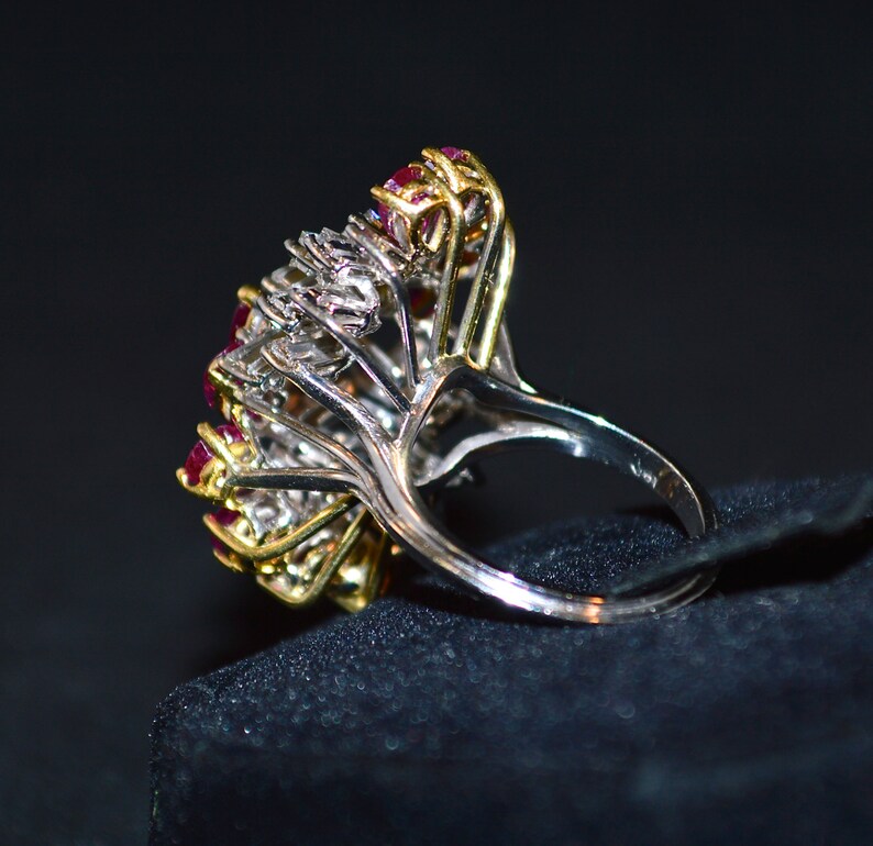 May include: A silver and gold ring featuring a cluster of red rubies and white diamonds. The ring is displayed on a black velvet background.