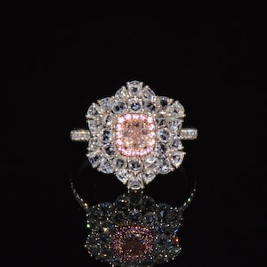 Puede incluir: Un anillo de plata con una gran piedra preciosa rosa y blanca rodeada de piedras blancas m&aacute;s peque&ntilde;as. El anillo est&aacute; engastado en un dise&ntilde;o con forma de flor.