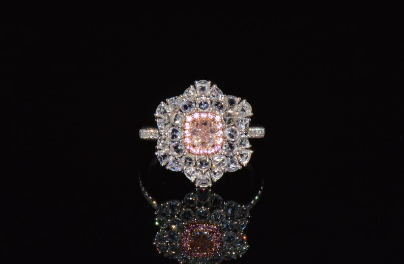Puede incluir: Un anillo de plata con una gran piedra preciosa rosa y blanca rodeada de piedras blancas m&aacute;s peque&ntilde;as. El anillo est&aacute; engastado en un dise&ntilde;o con forma de flor.