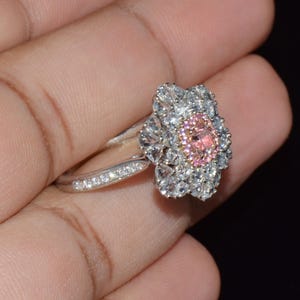 Puede incluir: Un anillo de plata con un dise&ntilde;o de flor rosa y blanca. La flor tiene una piedra central rosa grande rodeada de piedras blancas m&aacute;s peque&ntilde;as.