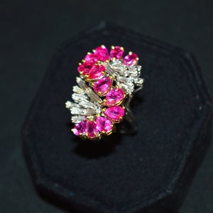 May include: A ring featuring a cluster of pink sapphires and baguette-cut diamonds set in a white metal band.