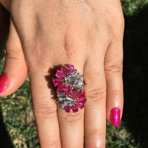 May include: A ring featuring a cluster of pink gemstones and baguette-shaped diamonds set in a gold band.