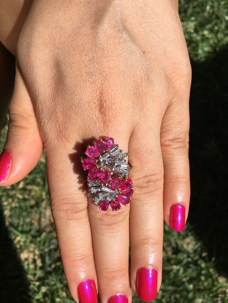 May include: A ring featuring a cluster of pink gemstones and baguette-shaped diamonds set in a gold band.