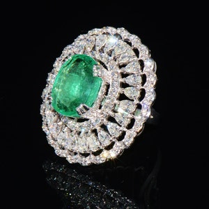 May include: A ring featuring a large, oval emerald gemstone set within a delicate, intricate design of smaller diamonds.