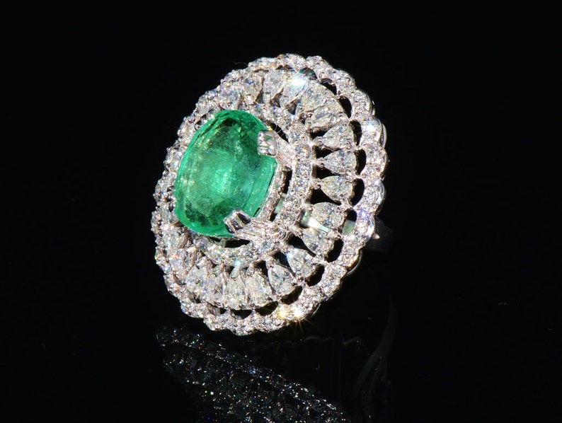 May include: A ring featuring a large, oval emerald gemstone set within a delicate, intricate design of smaller diamonds.